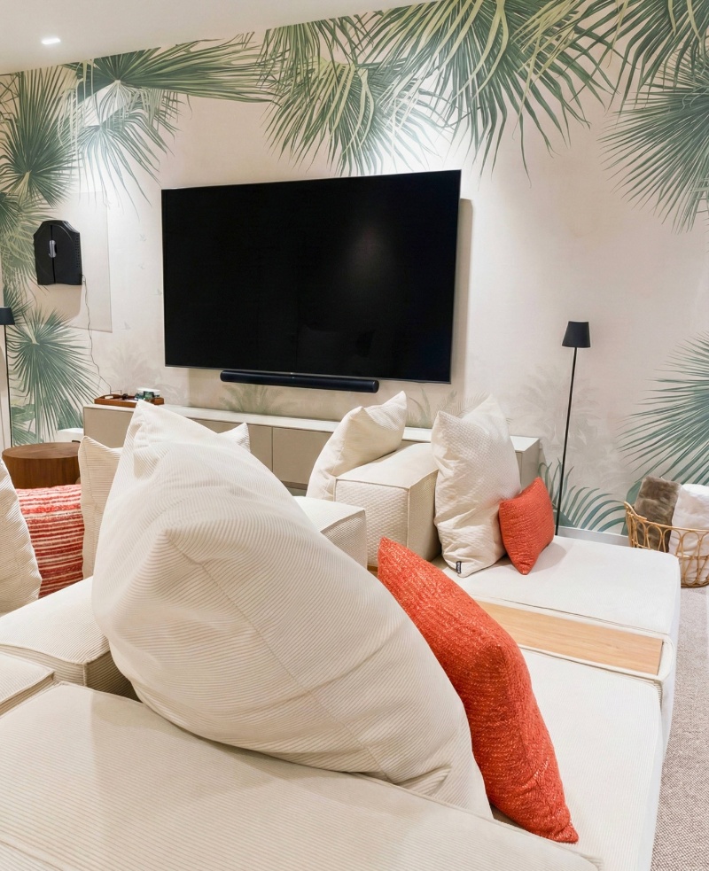 Salón de vivienda con sofá, cojines decorativos y papel pintado tropical en proyecto de interiorismo